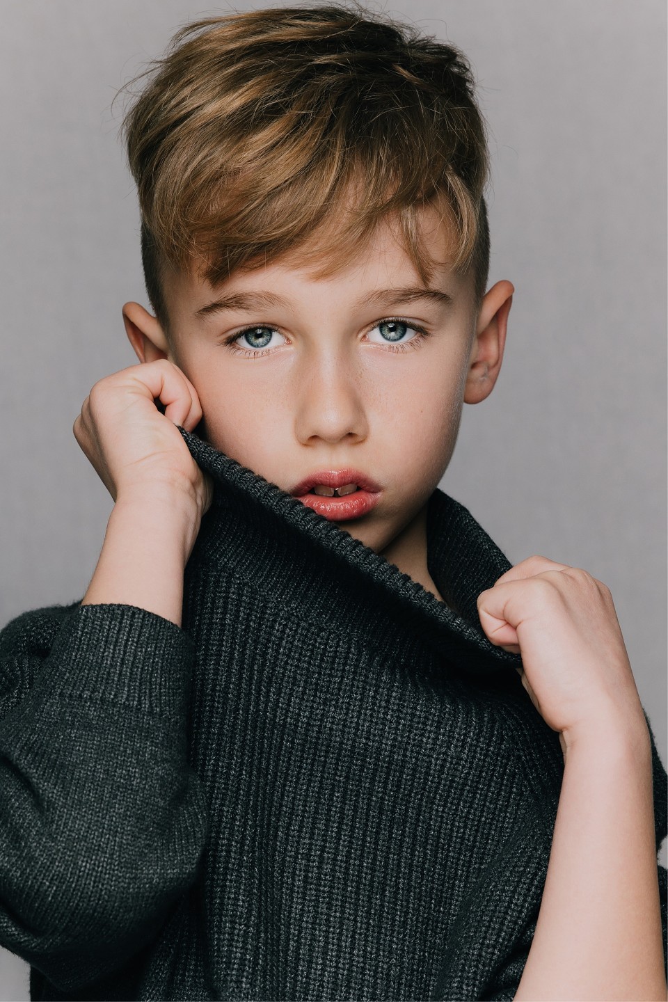 Young boy model pulling up the collar of a dark knit jumper