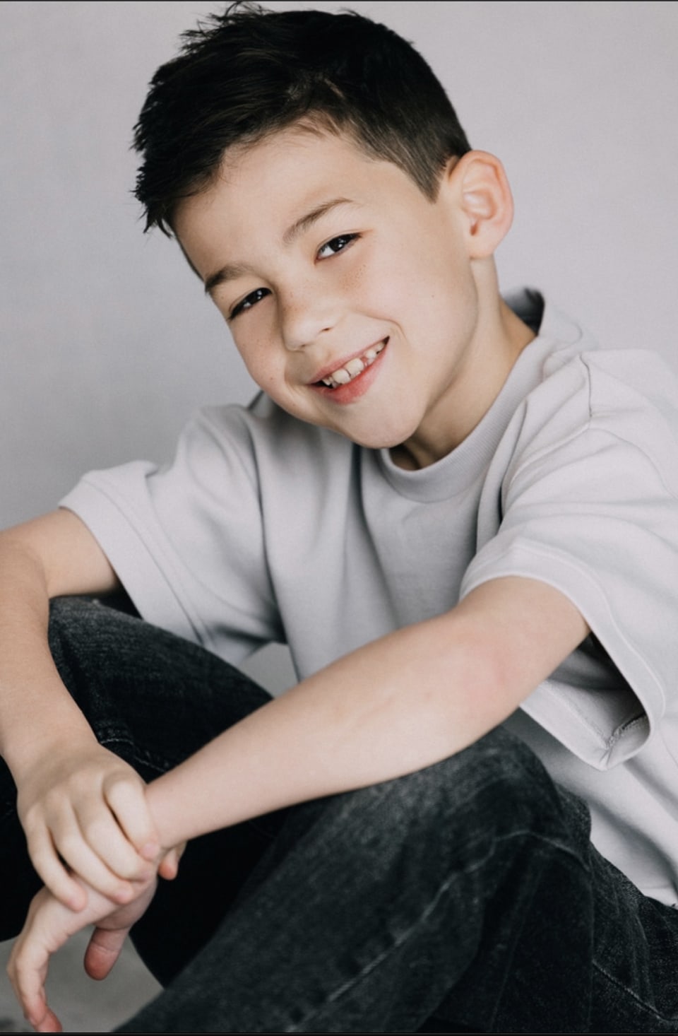 Smiling young boy model in a light grey t-shirt and dark jeans